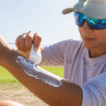 Athlete in cap, UV sunglasses and UPF shirt applying sunscreen in the sun