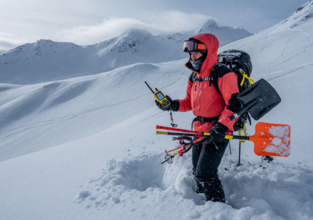 Backcountry skier holding an avalanche transceiver, probe and shovel in deep snow on a mountain slope