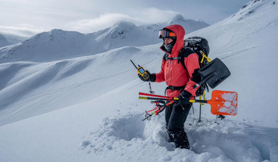 Backcountry skier holding an avalanche transceiver, probe and shovel in deep snow on a mountain slope