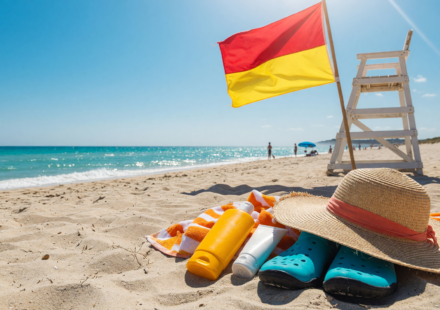 Beach with a warning flag on a lifeguard stand, sunscreen and water shoes
