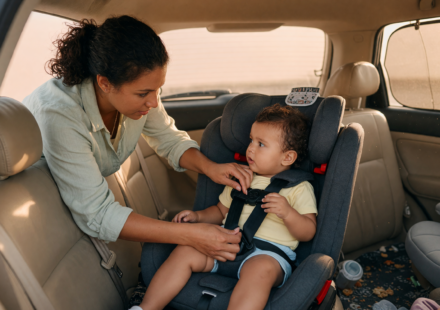 Parent securing a young child into a car seat in the back seat and checking the harness