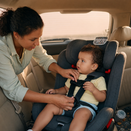 Parent securing a young child into a car seat in the back seat and checking the harness