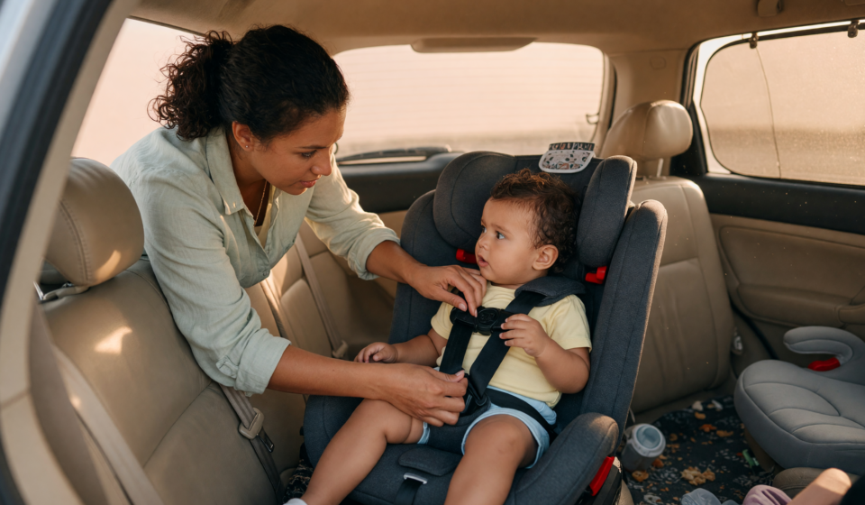 Parent securing a young child into a car seat in the back seat and checking the harness