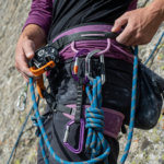 Close-up of a rock climber wearing a harness with belay device, locking carabiners and rope at a crag