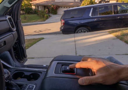 Pickup truck and SUV parked on a sloped driveway with a driver engaging the electronic parking brake
