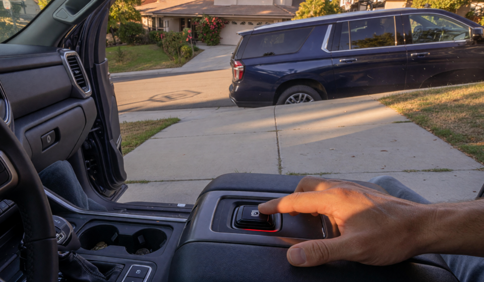 Pickup truck and SUV parked on a sloped driveway with a driver engaging the electronic parking brake