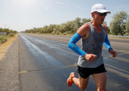 Runner in a vented cap and cooling arm sleeves on a sunny summer road
