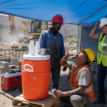 Construction workers at a shaded hydration station with an orange water cooler