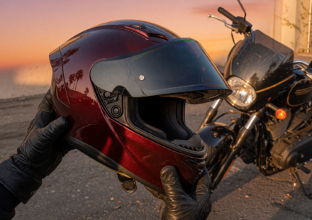 Full-face motorcycle helmet held in a rider's gloved hands beside a parked motorcycle at golden hour