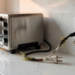 A stainless steel countertop electric toaster oven unplugged on a kitchen counter with focus on the power cord