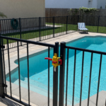 Backyard pool surrounded by a metal safety fence with a self-latching gate