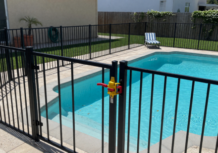 Backyard pool surrounded by a metal safety fence with a self-latching gate
