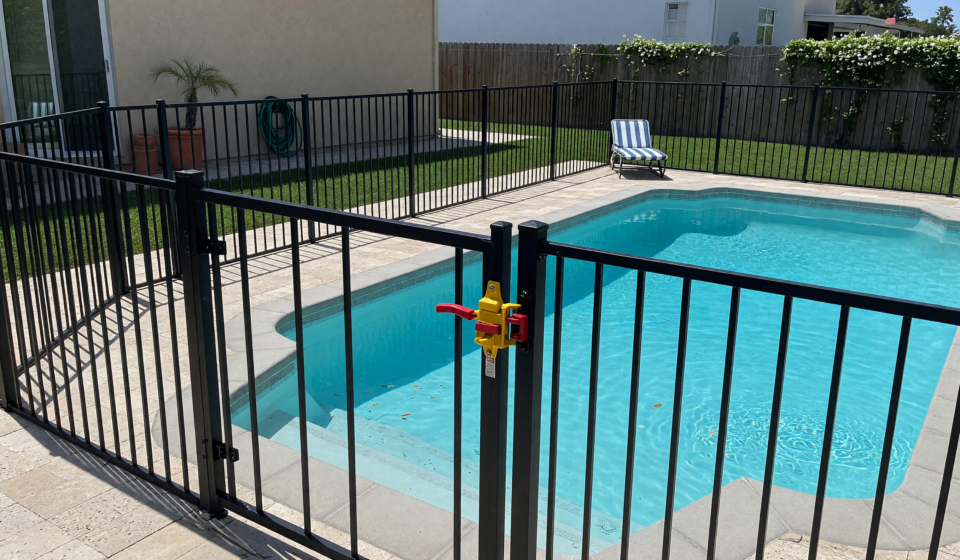Backyard pool surrounded by a metal safety fence with a self-latching gate