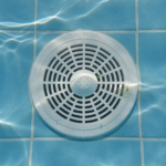 White circular pool drain cover on the tiled floor of a residential swimming pool underwater