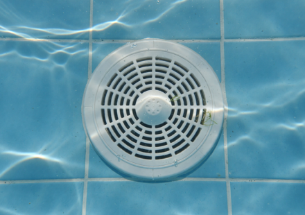 White circular pool drain cover on the tiled floor of a residential swimming pool underwater