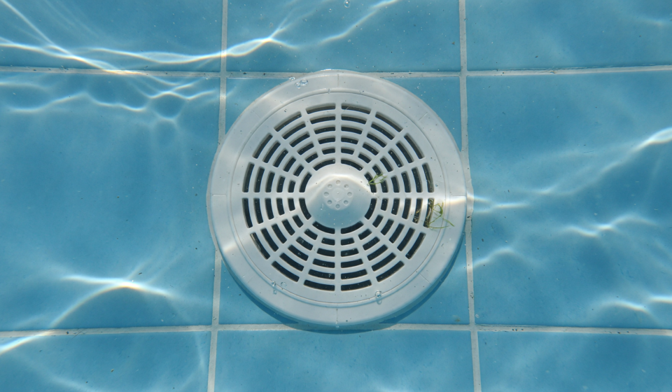 White circular pool drain cover on the tiled floor of a residential swimming pool underwater
