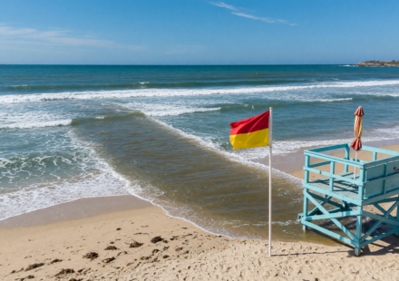 Ocean beach with a warning flag and lifeguard tower and a visible rip current channel cutting seaward