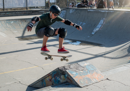 Skateboarder in helmet, wrist guards and knee pads mid-trick at a skatepark