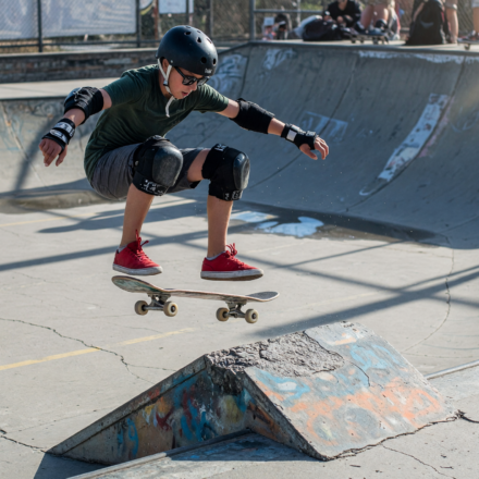 Skateboarder in helmet, wrist guards and knee pads mid-trick at a skatepark