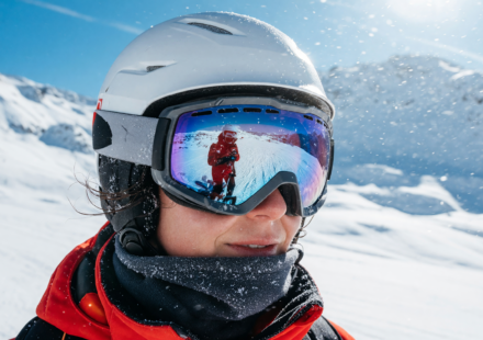 Skier wearing a helmet and snow goggles on a bright snowy mountain, close-up portrait
