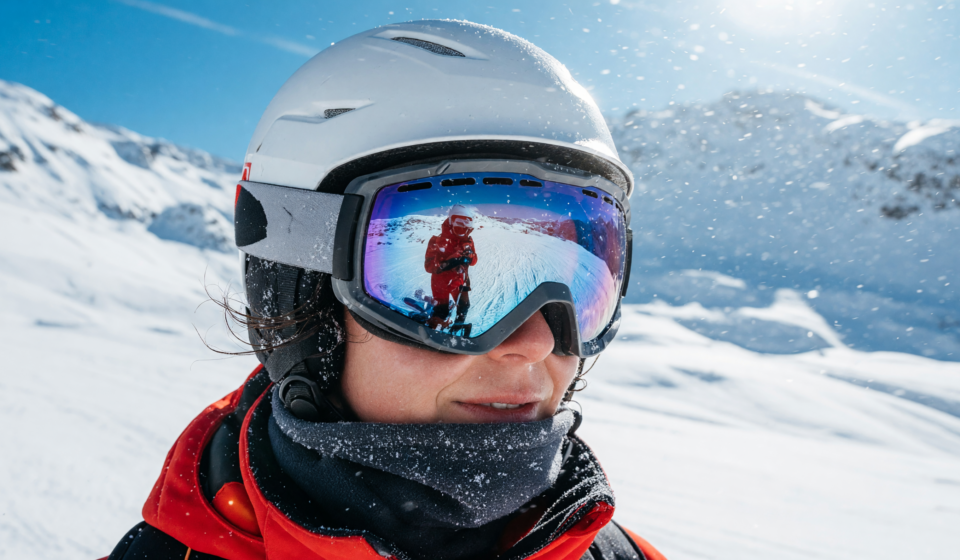 Skier wearing a helmet and snow goggles on a bright snowy mountain, close-up portrait