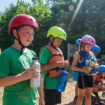 Children at summer camp wearing bike helmets with water bottles
