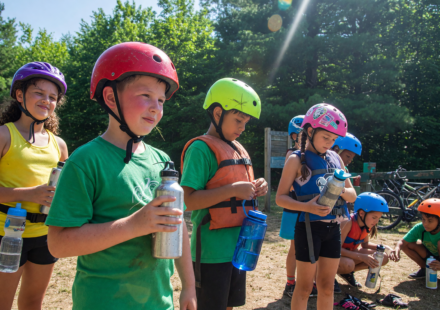Children at summer camp wearing bike helmets with water bottles