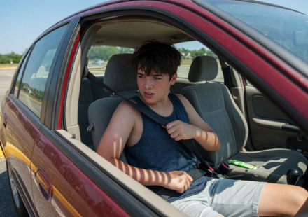 Teenage driver buckling a seatbelt inside a car on a summer day