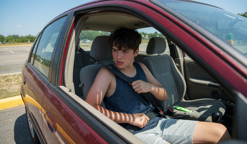 Teenage driver buckling a seatbelt inside a car on a summer day