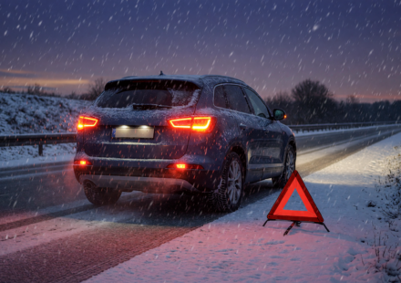 Car pulled safely onto a snowy roadside at dusk with hazard lights and a reflective warning triangle in falling snow
