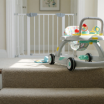A baby walker near the top edge of a carpeted staircase, illustrating the fall hazard behind the Kmaier infant walker recall