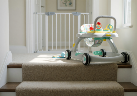 A baby walker near the top edge of a carpeted staircase, illustrating the fall hazard behind the Kmaier infant walker recall