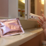 A foil numbing wipe packet on a bathroom counter beside a medicine cabinet with a child reaching in the background