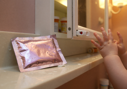 A foil numbing wipe packet on a bathroom counter beside a medicine cabinet with a child reaching in the background