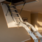 A folding pull-down attic stairway ladder extended from a ceiling hatch in a home hallway