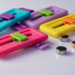 Small colorful silicone fidget slider toys beside tiny round magnets on a white surface
