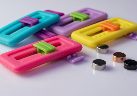 Small colorful silicone fidget slider toys beside tiny round magnets on a white surface