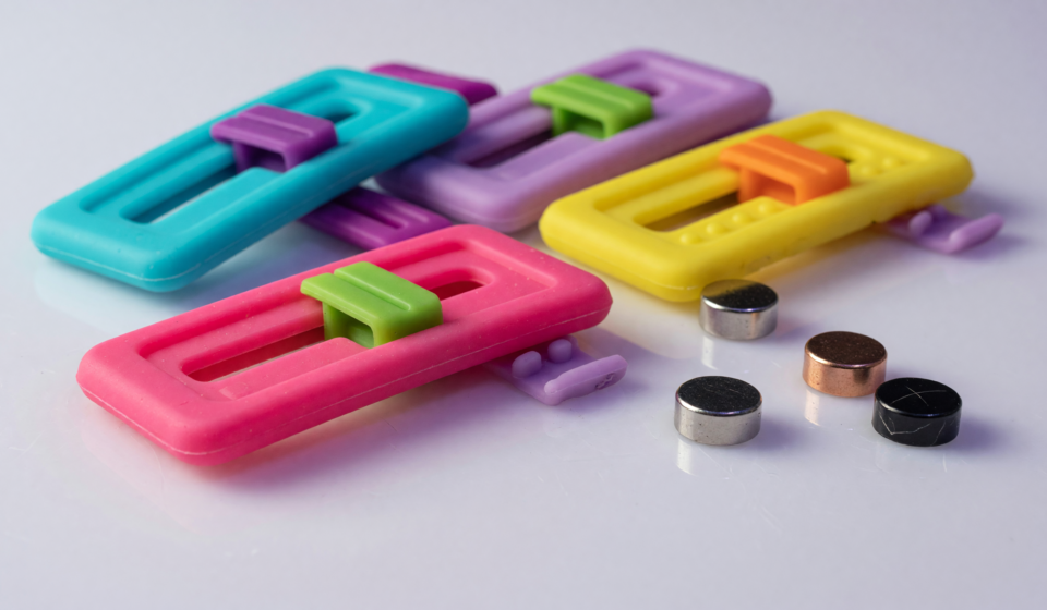 Small colorful silicone fidget slider toys beside tiny round magnets on a white surface