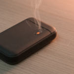 A rechargeable electronic hand warmer on a table with a wisp of smoke, illustrating the OCOOPA fire and burn hazard recall
