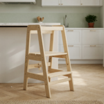 A natural wood foldable toddler tower stool standing empty on a kitchen floor next to a counter