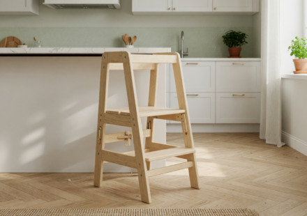 A natural wood foldable toddler tower stool standing empty on a kitchen floor next to a counter