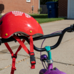 A child's red bicycle helmet resting on the handlebars of a kids bike in a driveway