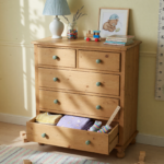 A tall six-drawer wooden dresser against a wall in a child's room with a lower drawer open, illustrating tip-over hazard