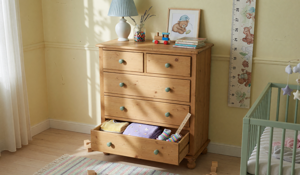 A tall six-drawer wooden dresser against a wall in a child's room with a lower drawer open, illustrating tip-over hazard