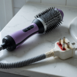 A hair dryer brush on a bathroom vanity beside a sink, showing the block-shaped safety plug that provides immersion protection