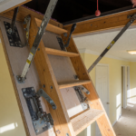 A pull-down attic stairway ladder unfolded into a home hallway, showing the hinge bolts and hardware at the center of the recall