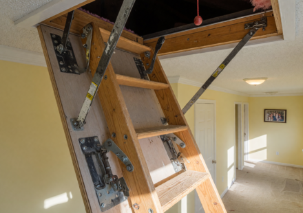 A pull-down attic stairway ladder unfolded into a home hallway, showing the hinge bolts and hardware at the center of the recall