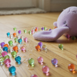 Colorful gel water beads spilled on a wooden floor beside a child's plush toy