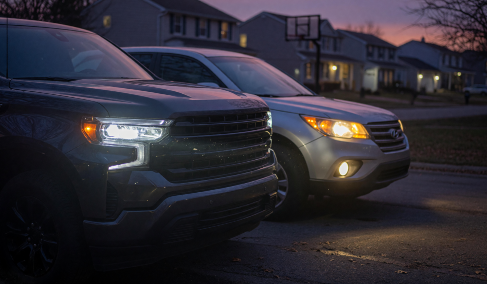 A pickup truck and SUV at dusk with one dim headlight and one bright, illustrating the Ford headlight recall visibility hazard