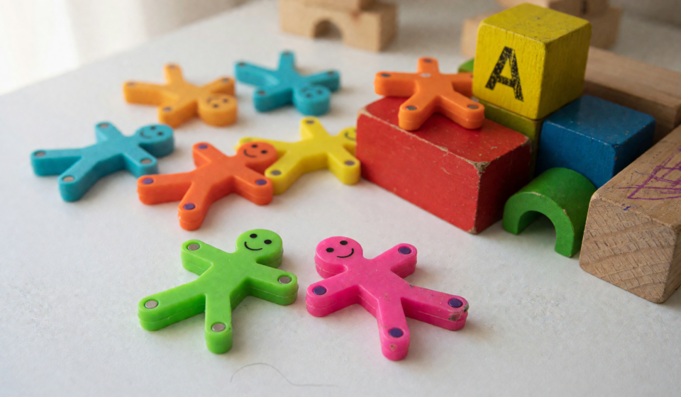 Small colorful magnetic stick figure toys scattered beside wooden building blocks, illustrating a magnetic toy recall over magnet ingestion risk